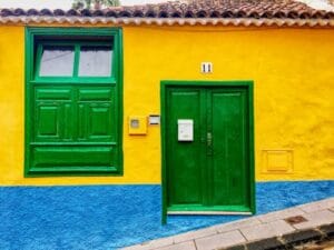 Vibrant yellow and blue facade with green door and window in Spanish village. Programa Casa Verde e Amarela.
