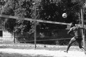 Black and white photo of a futevôlei player hitting a ball on a sandy court in Ilhéus, Brazil. Bola de Futebol.