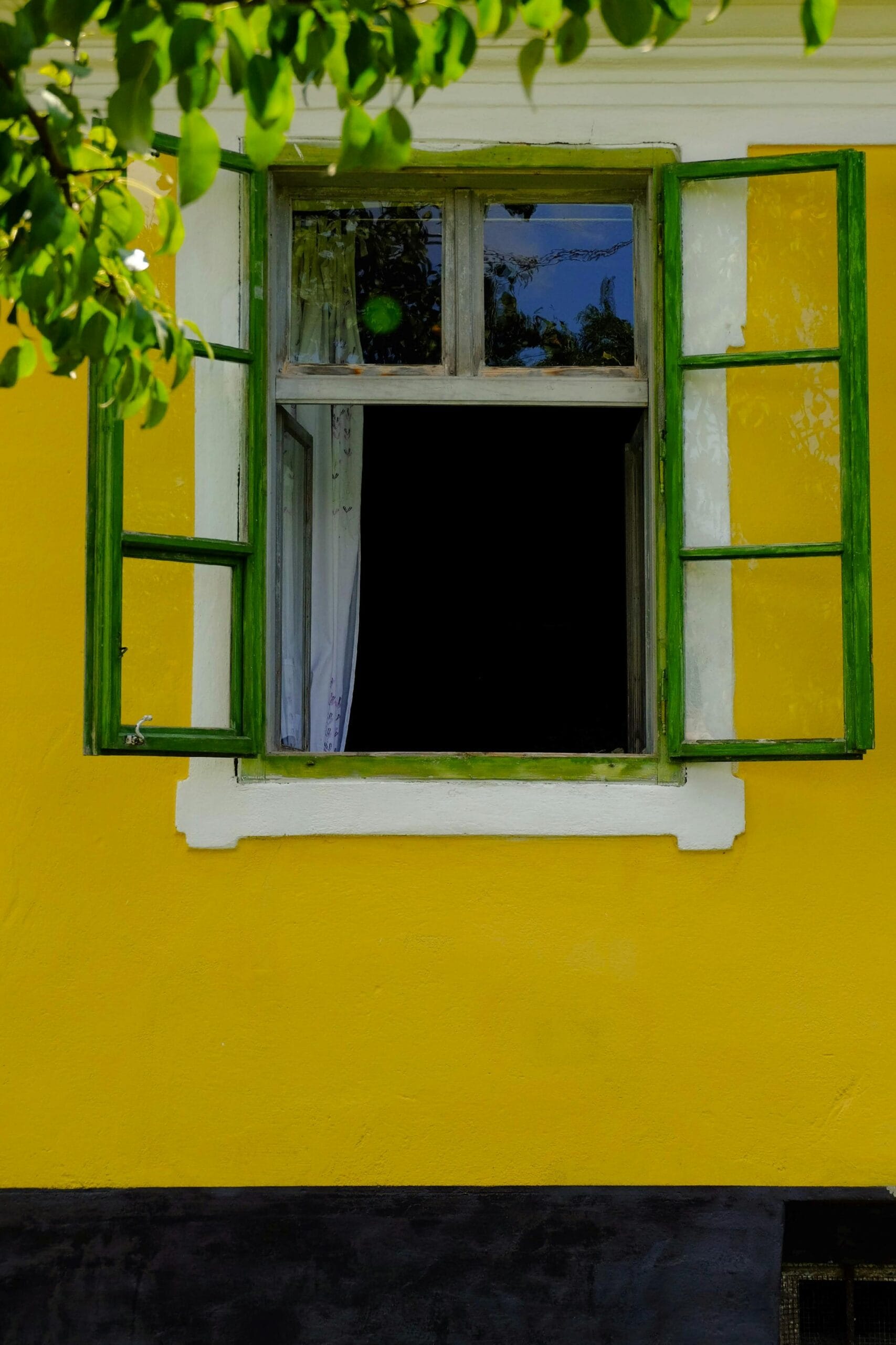 Bright yellow house with open green-framed window, inviting daylight and vibrant charm.