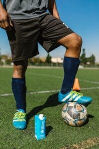 Soccer player preparing for practice on sunny field with ball and water carton. Bola de Futebol.