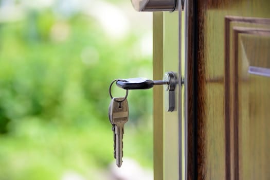 Key inserted in door lock against a blurred green background, symbolizing security and real estate. Casa dos Sonhos.
