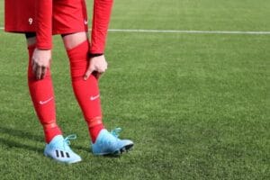 A soccer player in red uniform adjusting socks on a green grass field. Football boot, Chuteiras.