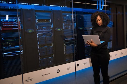 A female engineer using a laptop while monitoring data servers in a modern server room. Technology, Tecnologia.
