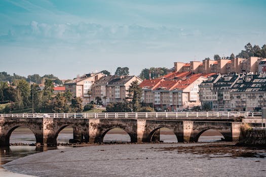 Picturesque view of a historic bridge and vibrant buildings in Cambre, Galicia, Spain under a clear blue sky. Casas para Alugar.