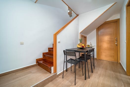 Clean and minimalist interior with wooden accents, featuring a small dining area under the stairs. Casa Manutenção preventiva.