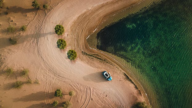 Aerial shot of a sandy beach, water, and parked car in Dubai. Trip, Viagem.