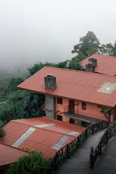 A rustic house with red roof nestled in a misty jungle environment, showcasing tropical nature.Casa Verde Amarela.