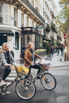 Two women cycling on a city street on a clear day, showcasing urban life. Cycling, Ciclismo.