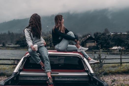 Two young women sitting on a car, enjoying the serene mountain landscape in Romania. Trip, Viagem.