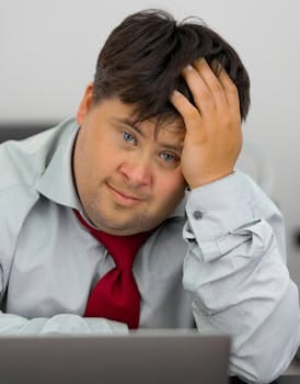 A man deeply in thought while working at his office desk, displaying focus and contemplation. Jobs, Empregos.