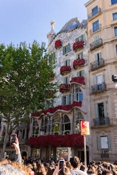 Crowd gathered at Casa Batlló in Barcelona with building adorned in red roses for Sant Jordi celebration. casa.