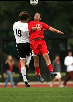 Two soccer players in mid-air challenge on a green field during a game. Soccer, Futebol.