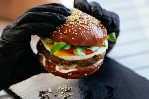 Mouth-watering cheeseburger with lettuce, tomato, and sesame bun held by hands in gloves. Food, comida, Meat and sesame food.