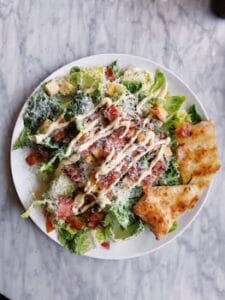 Tasty Caesar salad topped with bacon, cheese, and drizzled sauce, served with crispy bread. Food, Comida.