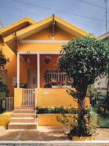 Bright yellow house with lush garden, vibrant flowers, and welcoming porch entrance. Home, casa.