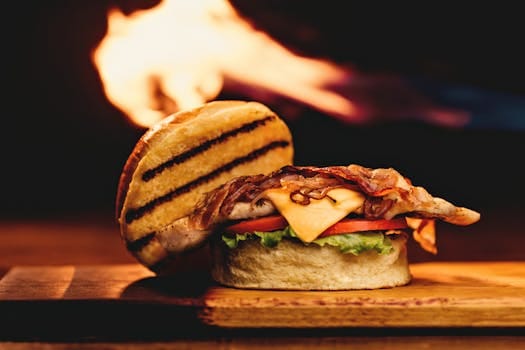 Close-up of a mouth-watering grilled bacon and cheese burger on a wooden board with a fiery background. Bacon recipes, Receitas de bacon.