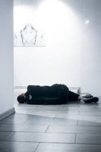 A man in casual wear lying on a tile floor in a bright, modern gallery. Anxiety, Ansiedade.