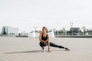 Young woman in black sportswear stretching outdoors in a sunny urban environment. Kegel exercises, Exercícios de Kegel.