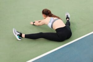 Young woman in activewear stretching on a tennis court for workout. Kegel exercises, Exercícios de Kegel.