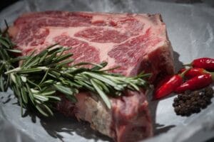 Close-up of a raw steak garnished with rosemary and chilies, ideal for cooking concepts. Meats, Carnes.