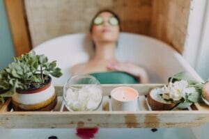 Woman relaxing in a bathtub with a candle and plants, enjoying a serene spa experience. Nuru massage, Massagem Nuru.
