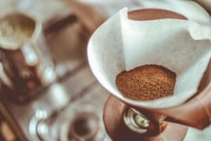 A close-up of ground coffee in a pour-over filter on a stovetop background, ideal for coffee enthusiasts. Filtered Coffee, Café Coado.