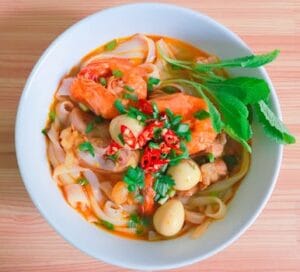 A vibrant bowl of Vietnamese noodle soup with shrimp, herbs, and quail eggs. Food, comida.