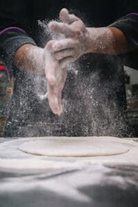 A chef clapping hands over dough, releasing flour in a kitchen setting.Food, comida.