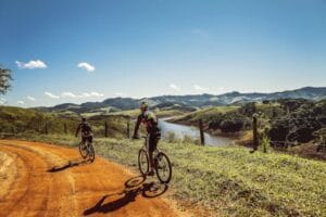 Two cyclists riding on a dirt trail with stunning mountain views and clear skies. Ciclismo, Cycling.