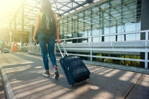 A woman walks with a suitcase outside an airport terminal, ready for travel. Trip, viagem.