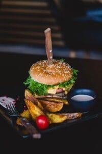 Close-up of a gourmet cheeseburger with wedges and tomato on a black plate. comida, Food x burger, food.