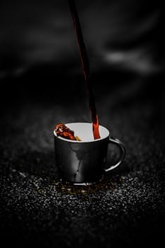 Close-up of steaming dark coffee being poured into a black cup on a dark textured surface. Rich aroma. Café, Coffee, comida, food.