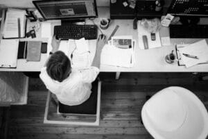 Black and white image of an employee working at a desk with papers and computer. Emprego, Job.