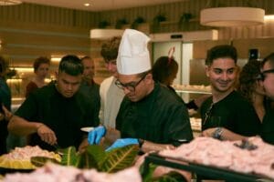 A chef in glasses serves food to guests at a lively indoor buffet event. Calabrian food, food, comida.