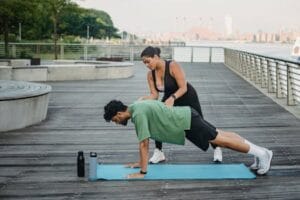 A man and woman engaging in a fitness workout on a riverside boardwalk, featuring stretching and push-ups.Health training, saúde.