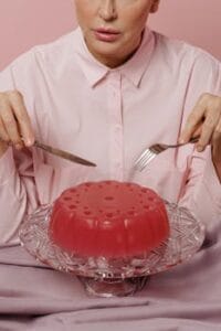 An elegant pink jelly dessert on a cake stand with a woman about to enjoy it. pudding food, food, comida.