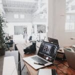 A bright, modern workspace featuring laptops, a camera, and a drawing tablet in an indoor office. Technology, Tecnologia.