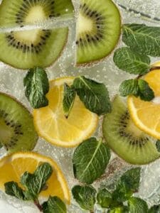 Vibrant citrus and kiwi slices with mint leaves in a sparkling beverage viewed from above. Health Detox, Saúde Detox.