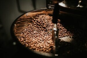 Close-up of freshly roasted coffee beans in a large industrial coffee roaster, showcasing rich textures and warm tones. Coffee food, comida, food, 